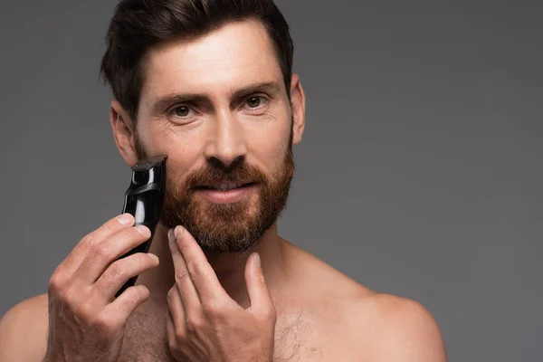 Без рубашки мужчина с волосами на груди бритья бороду с электрической бритвой изолированы на сером — стоковое фото