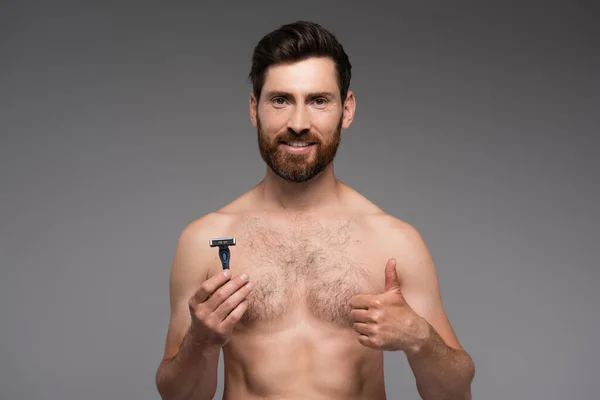 Happy bearded man holding safety razor and showing thumb up isolated on grey — Stockfoto