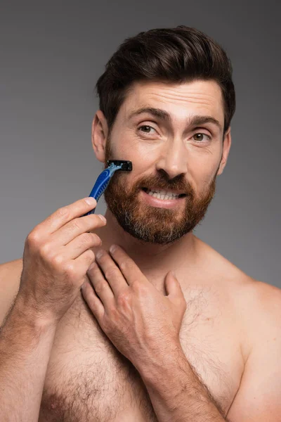 Portrait of shirtless man shaving beard with safety razor isolated on grey — Stockfoto