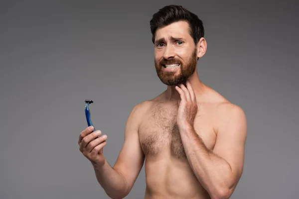 Displeased and shirtless man with beard holding safety razor isolated on grey - foto de stock