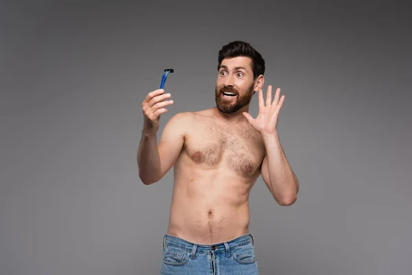 Scared and shirtless man with beard holding safety razor isolated on grey - foto de stock