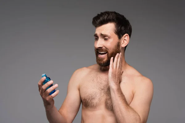 Bearded and shirtless man holding bottle with after shave product isolated on grey — Stock Photo
