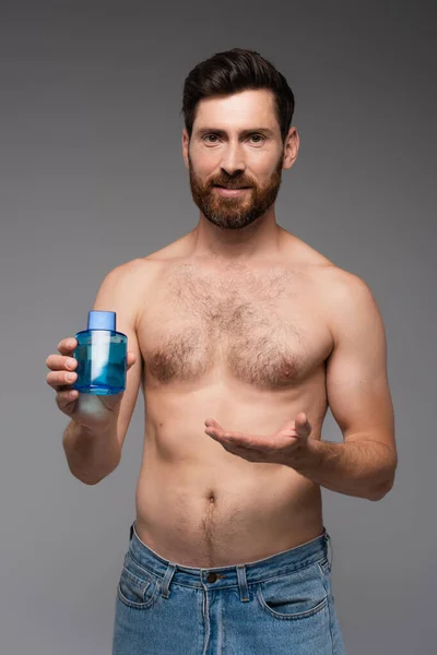 Бородатий і без сорочки чоловік вказує рукою в пляшці після гоління продукт ізольований на сірому — стокове фото