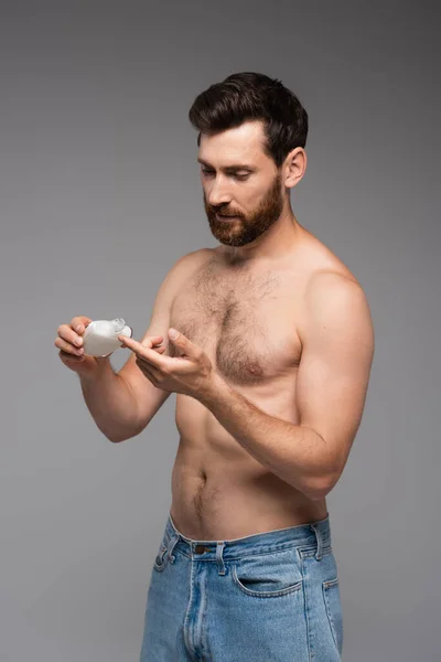 Shirtless man with beard holding bottle and pouring after shave product isolated on grey — Stock Photo