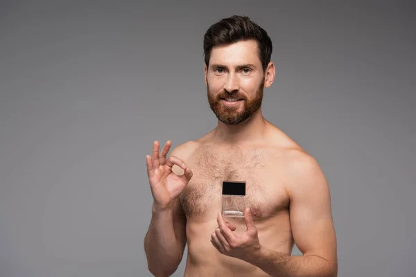 Happy and shirtless man holding bottle with perfume and showing ok sign isolated on grey — Foto stock