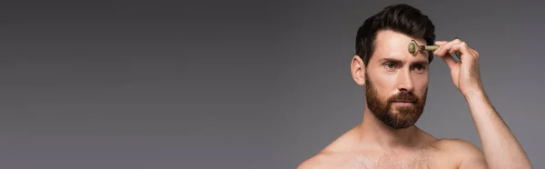 Shirtless man with beard using jade roller while massaging face isolated on grey, banner — Fotografia de Stock