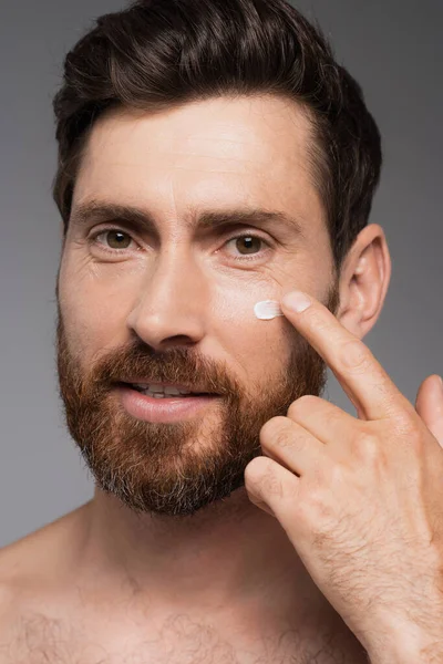 Close up of man with beard applying cream on face isolated on grey — Fotografia de Stock