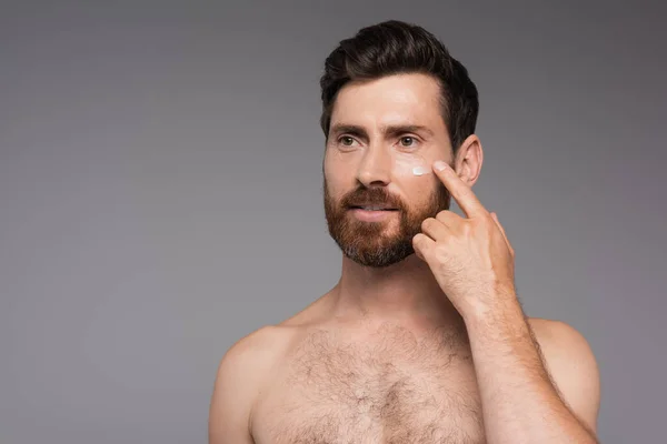 Bearded and shirtless man applying cream on face isolated on grey — Stock Photo