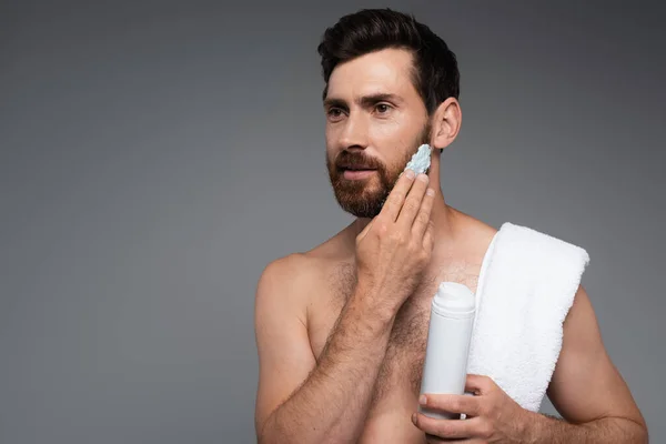 Bearded man with towel applying shaving foam isolated on grey — Stockfoto