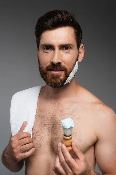 Bearded man with shaving foam on face holding shaving brush isolated on grey — Foto stock