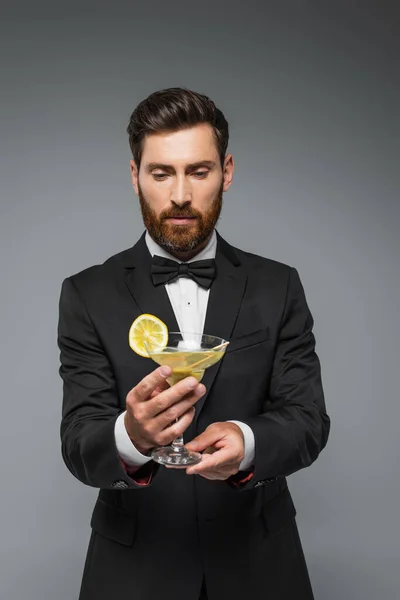 Bearded man in elegant suit with bow tie holding glass with cocktail isolated on grey — Stockfoto