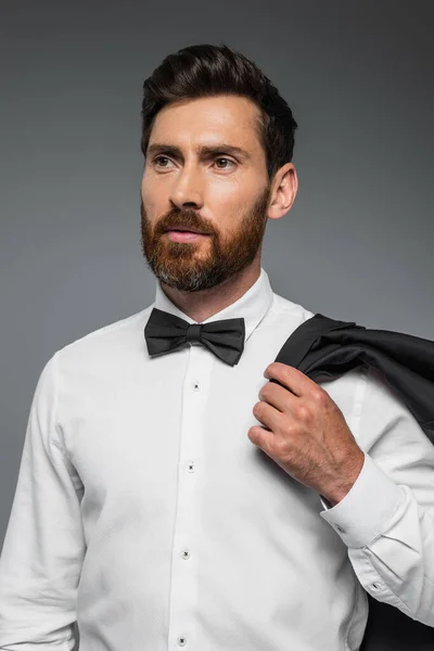 Portrait of bearded man in suit with bow tie holding blazer isolated on grey — Photo de stock