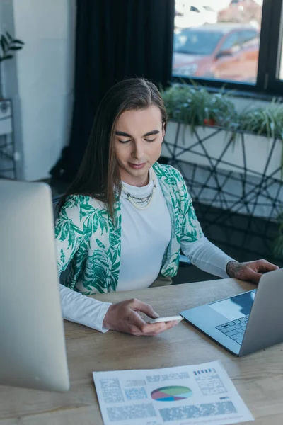 Queer designer using smartphone near devices and paper in office — Stock Photo