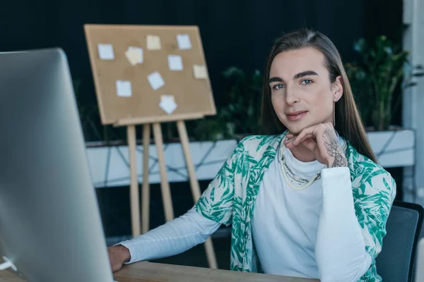 Tattooed queer designer looking at camera near computer in creative agency — Fotografia de Stock