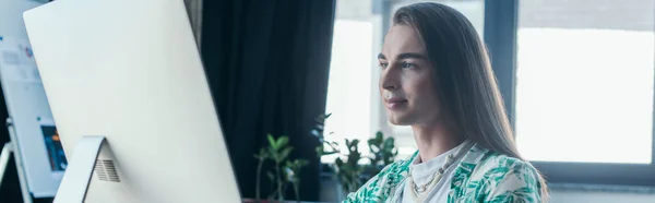 Nonbinary designer looking at computer monitor in office, banner — Stock Photo