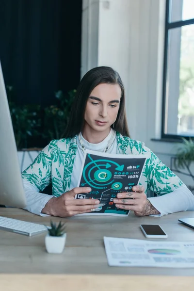 Queer designer looking at charts near devices in office — Stockfoto