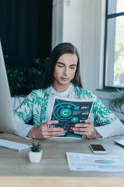 Queer designer looking at charts near devices in office - foto de stock