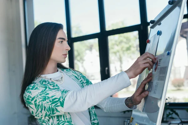 Side view of nonbinary designer looking at charts on flip chart in office — Stock Photo