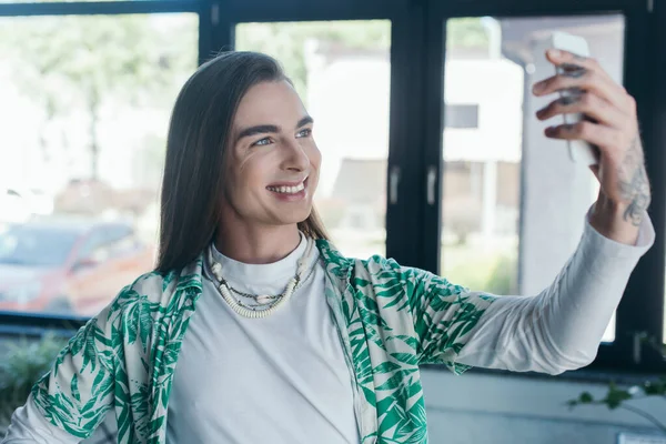 Cheerful queer designer using blurred smartphone in creative agency — Stock Photo