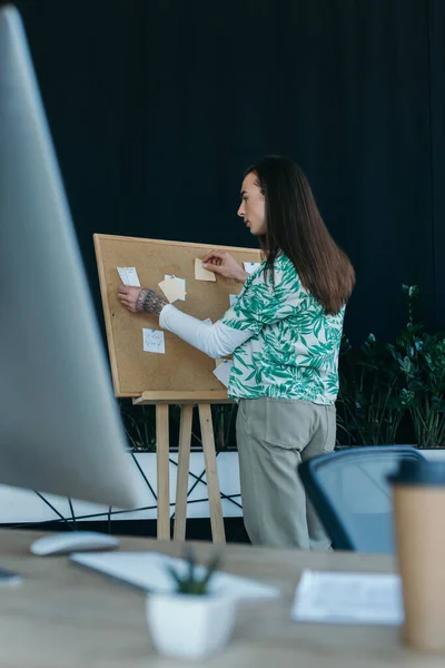 Side view of brunette queer designer working with sticky notes on board in office — Stock Photo