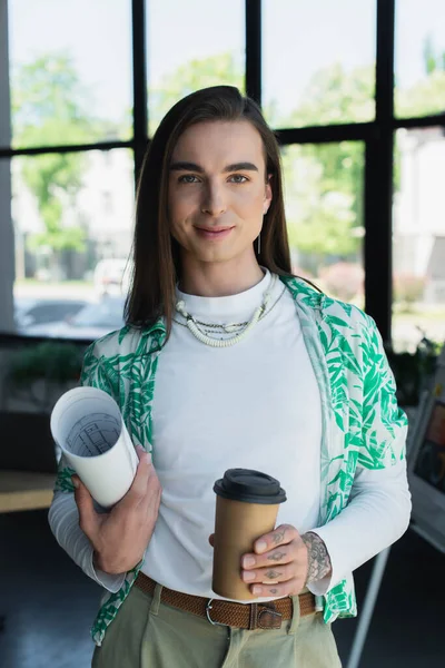 Smiling queer designer holding blueprint and coffee to go in office — Foto stock