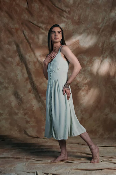 Full length of barefoot nonbinary person in dress standing on abstract background — Stockfoto