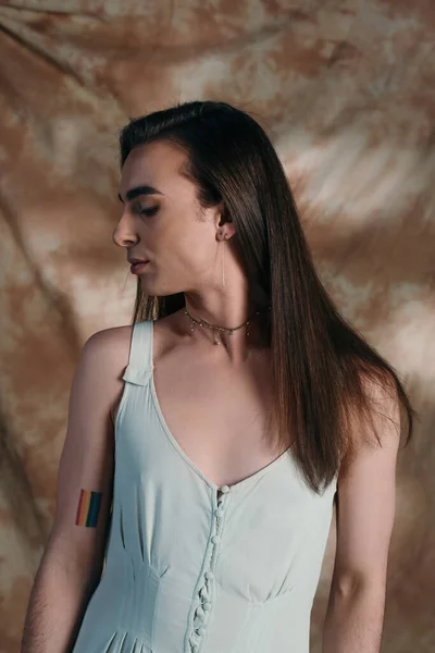 Side view of brunette queer person in dress standing on abstract background — Stock Photo