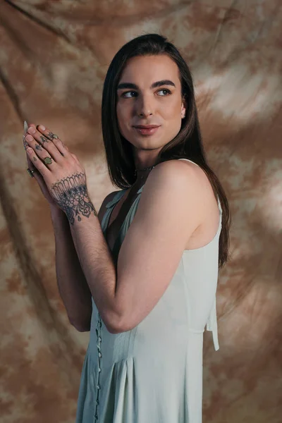 Smiling tattooed queer person in dress looking away on abstract background — Stock Photo