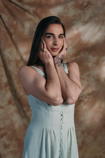 Nonbinary person in dress touching face and looking at camera on abstract background — Fotografia de Stock