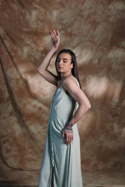 Stylish nonbinary person in dress posing with closed eyes on abstract background — Stockfoto