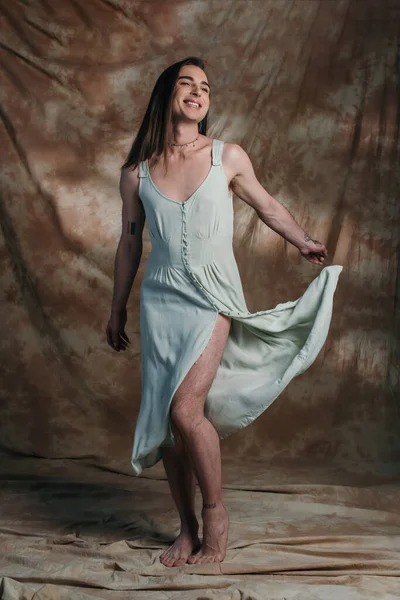 Full length of smiling queer person throwing dress on abstract brown background - foto de stock