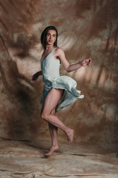 Positive queer person in sundress jumping and looking at camera on abstract brown background — Foto stock