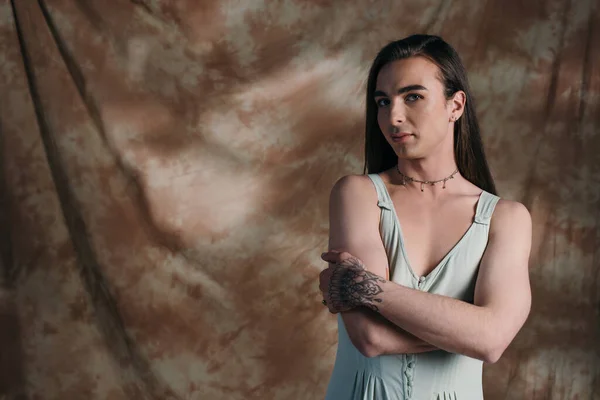 Young queer person in sundress looking at camera on abstract brown background - foto de stock