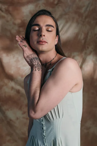 Портрет стильного странного человека в платье, позирующего на абстрактном коричневом фоне — стоковое фото