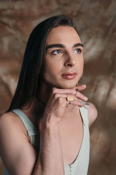 Portrait of stylish queer person with makeup looking away on abstract brown background — Stockfoto