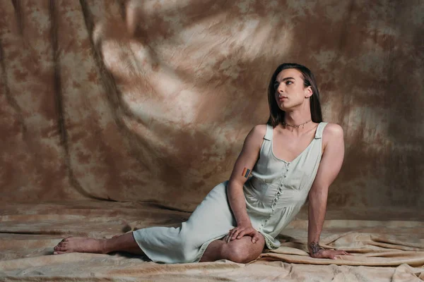 Brunette queer person in dress sitting on abstract brown background — Foto stock