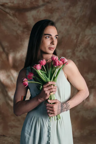 Молодой педик в сарафане держит тюльпаны на абстрактном коричневом фоне — стоковое фото