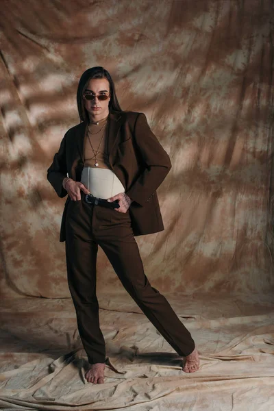 Barefoot queer person in suit and corset posing on abstract brown background — Stockfoto