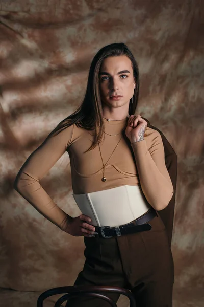 Fashionable queer person in corset holding blazer on abstract brown background — Stockfoto