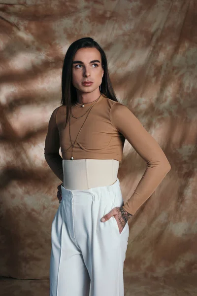 Trendy nonbinary person in corset posing on abstract brown background — Stockfoto