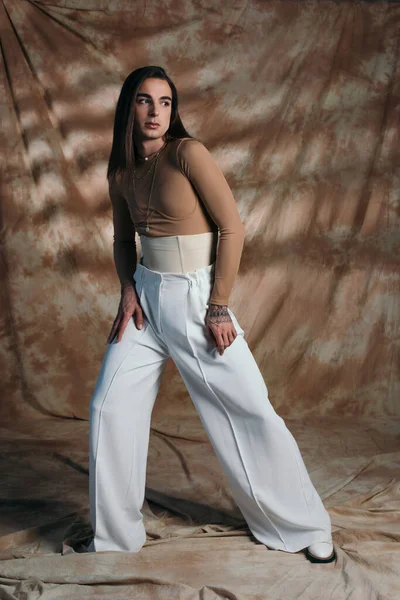 Full length of trendy nonbinary person standing on abstract brown background — Stockfoto