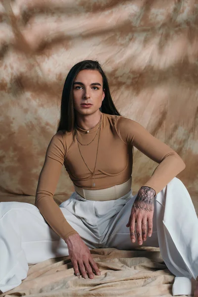 Fashionable queer person in corset and white pants looking at camera on abstract brown background — Stock Photo