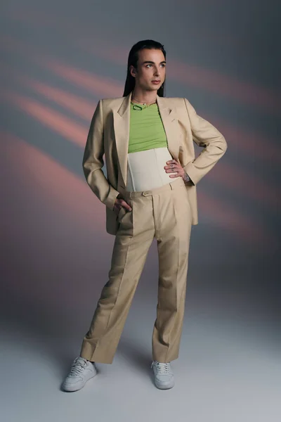 Full length of trendy queer person in suit standing on abstract background — Stockfoto