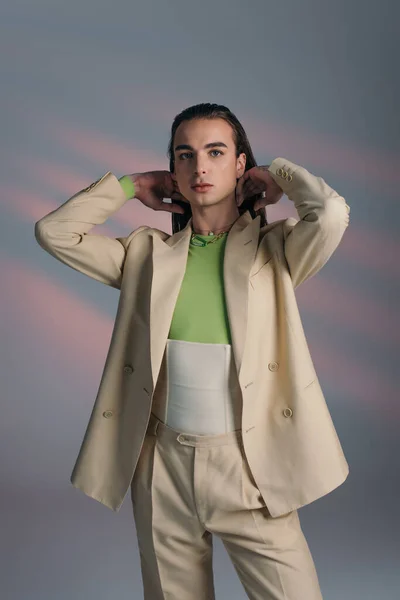 Fashionable queer person in beige suit and corset looking at camera on abstract background — Photo de stock