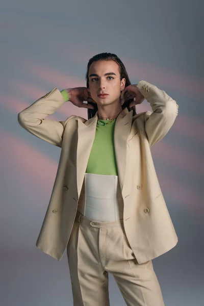 Fashionable queer person in beige suit and corset looking at camera on abstract background — Fotografia de Stock