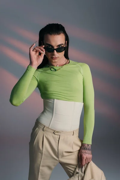 Young queer model holding sunglasses and jacket on abstract background — Photo de stock