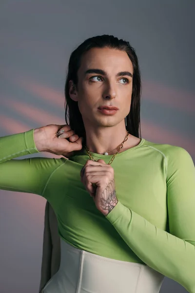 Trendy nonbinary model touching necklace and looking away on abstract background — Stock Photo