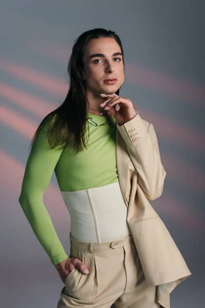 Trendy nonbinary model in suit looking at camera on abstract background — Foto stock