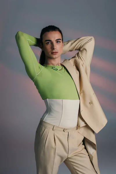 Trendy queer person in corset and jacket touching hair on abstract background — Foto stock