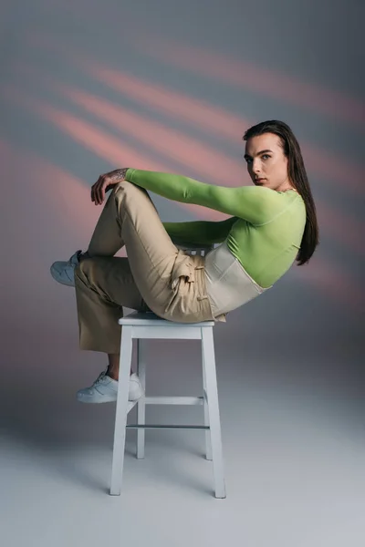 Stylish queer model posing on chair on abstract background — Stock Photo